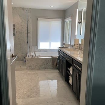 A finished bathroom remodel with a marble surround soaking tub, glass shower and dark vanity.