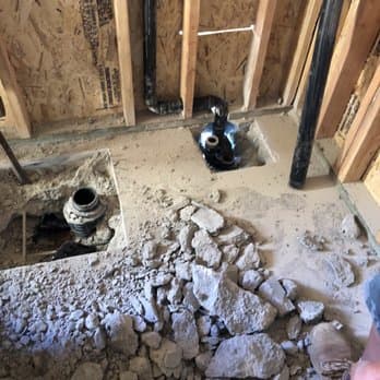 Bathroom rough-in plumbing: new drain and vent lines set into an opened slab between wall studs.
